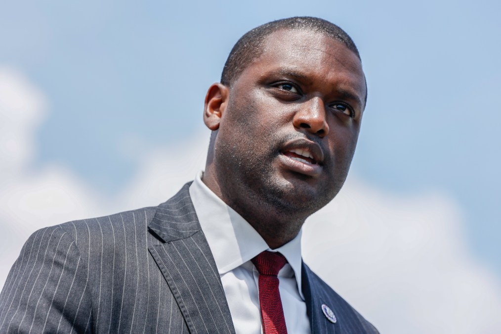 Mondaire Jones is pictured from the shoulders up with blue sky behind him. He is wearing a gray suit with a red tie.